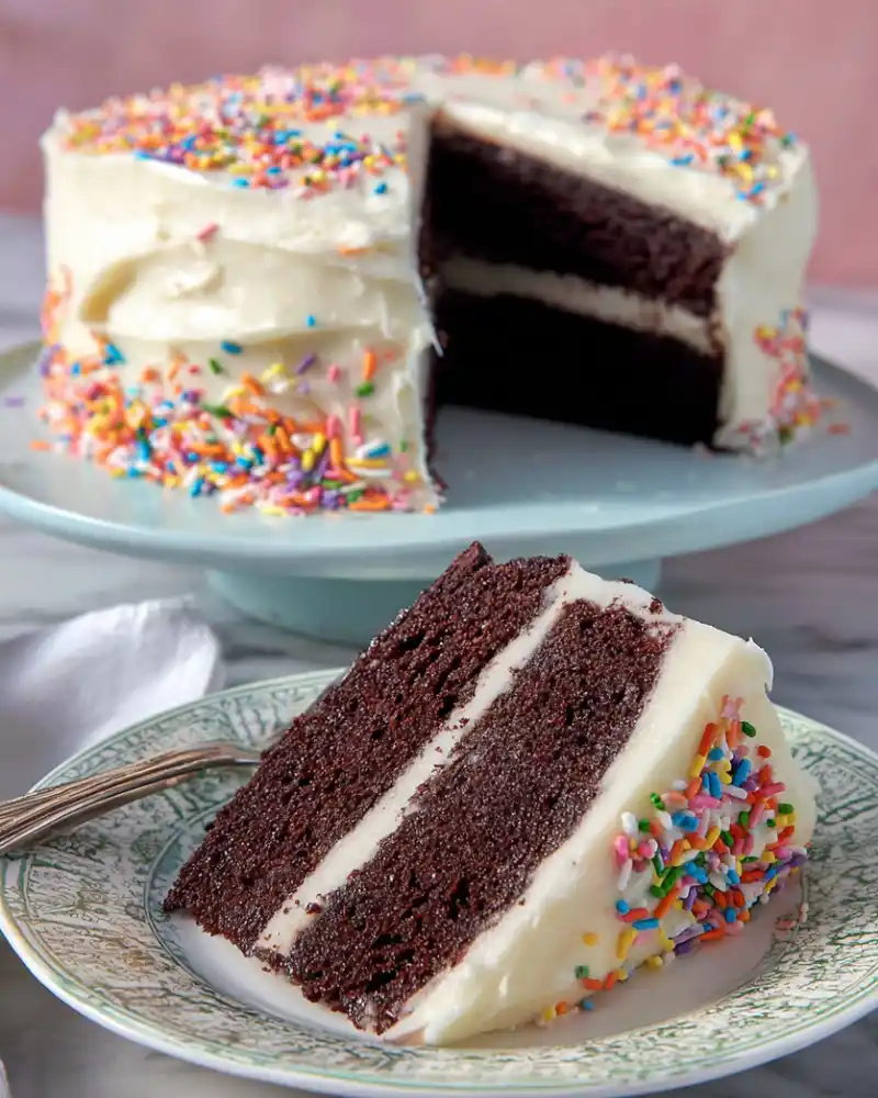 Slice of gluten-free chocolate cake with vanilla frosting on a plate.