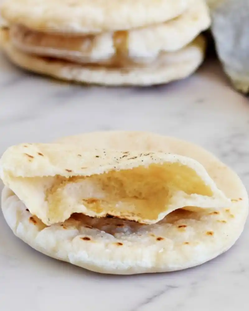 Gluten-free pita bread with a cut-open pocket showing a soft, fluffy inside on a marble surface.