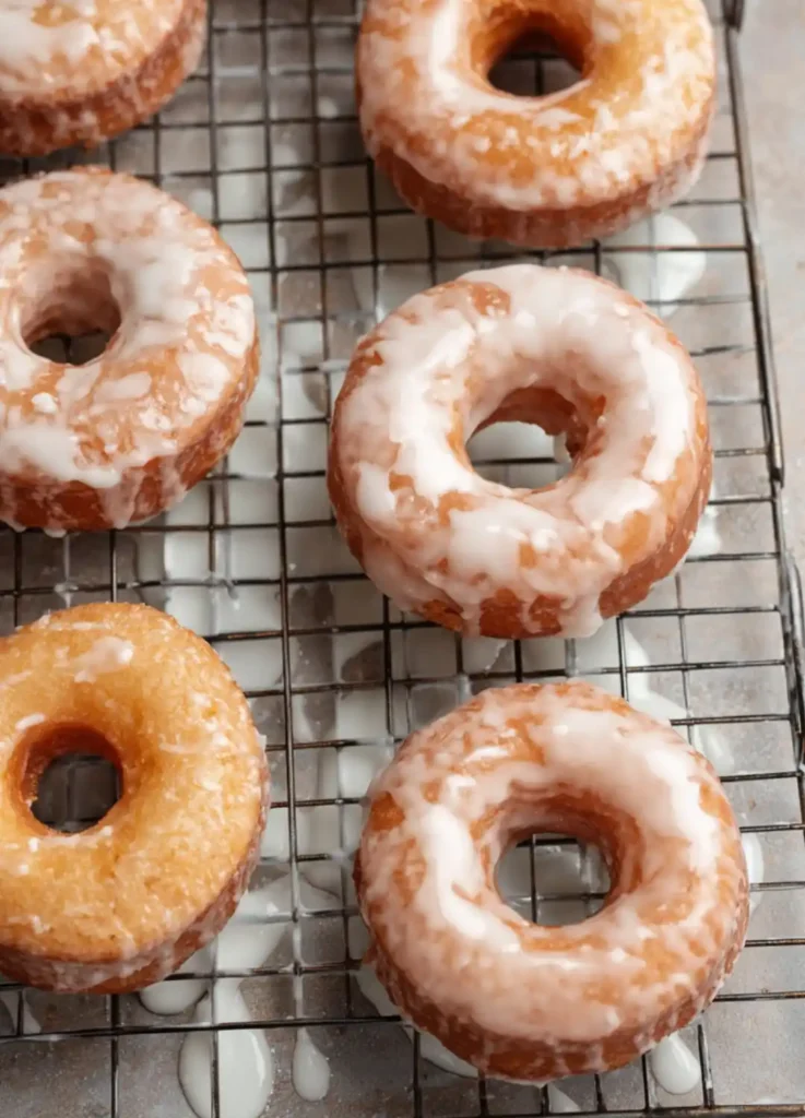 gluten-free glazed donuts cooling on a wire rack with vanilla icing dripping