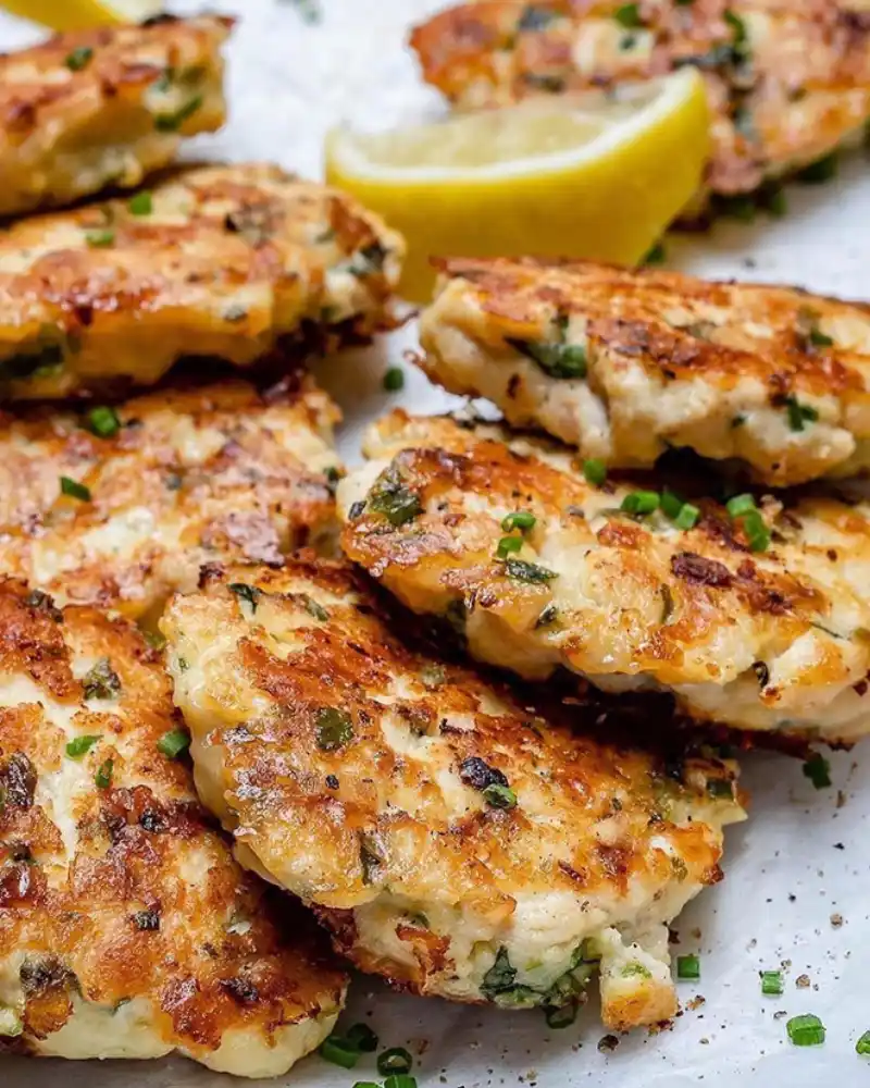 Gluten-free chicken fritters stacked on a plate, golden and crispy with herbs.