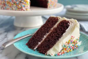 Slice of gluten-free chocolate cake with vanilla frosting on a plate.