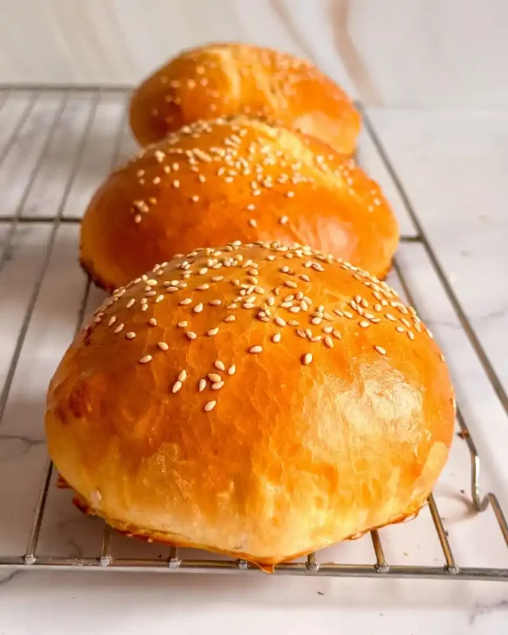 Soft gluten-free hamburger buns topped with sesame seeds on a baking tray.