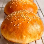 Soft gluten-free hamburger buns topped with sesame seeds on a baking tray.