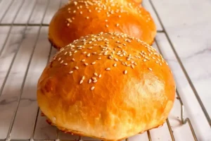 Soft gluten-free hamburger buns topped with sesame seeds on a baking tray.