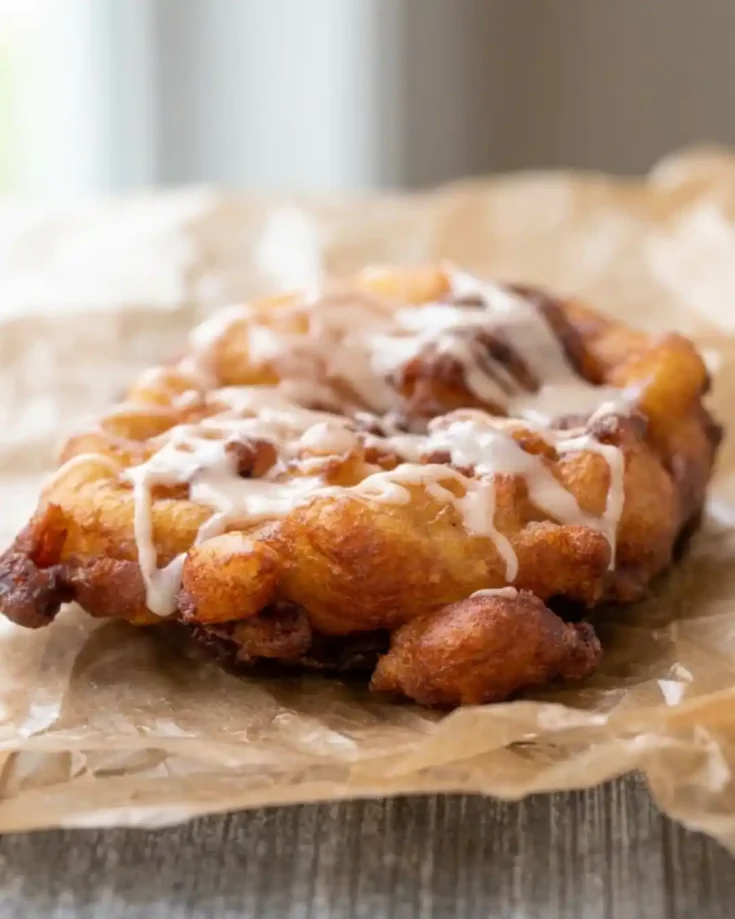 Gluten-free apple fritters drizzled with glaze and served on parchment paper.