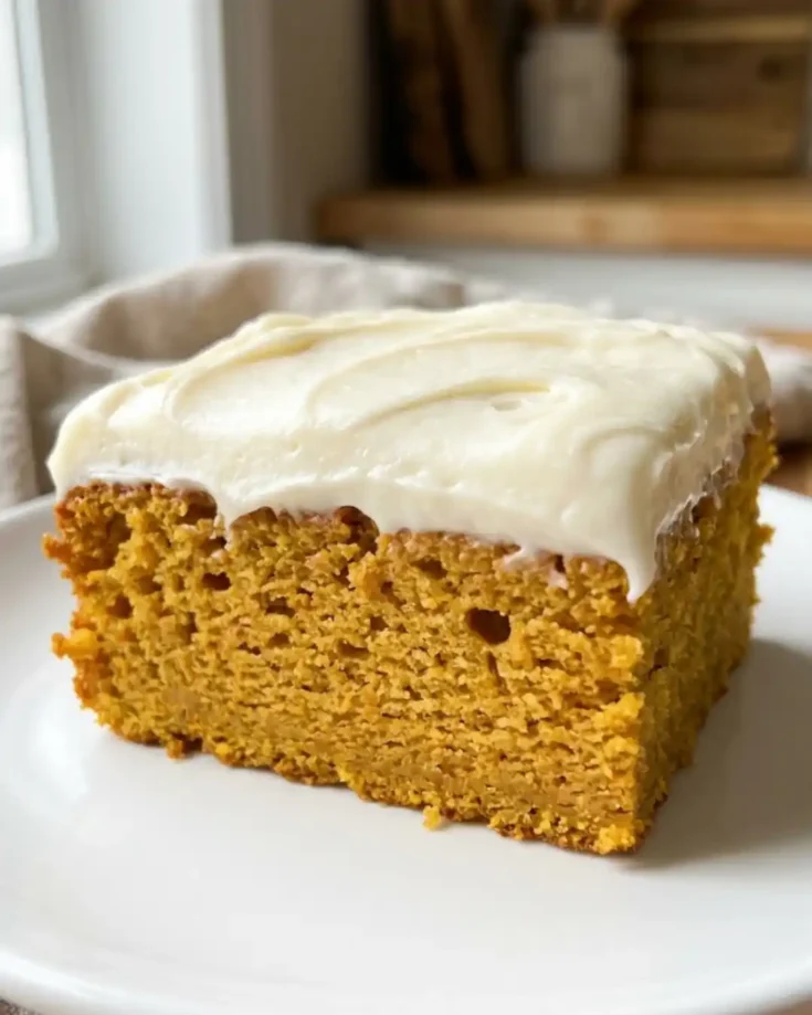 Slice of gluten-free pumpkin cake with thick cream cheese frosting on a white plate.