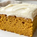 Slice of gluten-free pumpkin cake with thick cream cheese frosting on a white plate