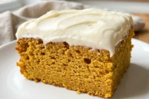 Slice of gluten-free pumpkin cake with thick cream cheese frosting on a white plate